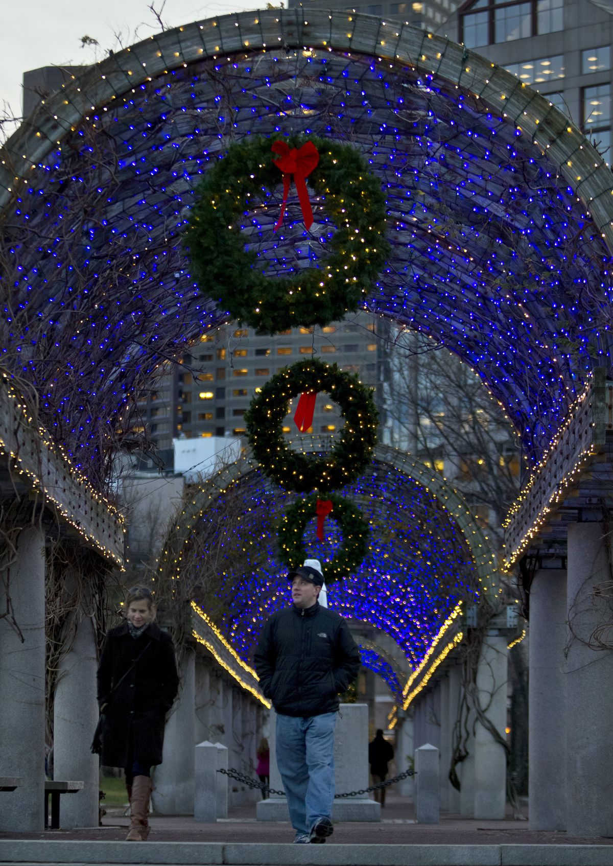 A trellis entwined with bright lights, and people are walking under the trellis.