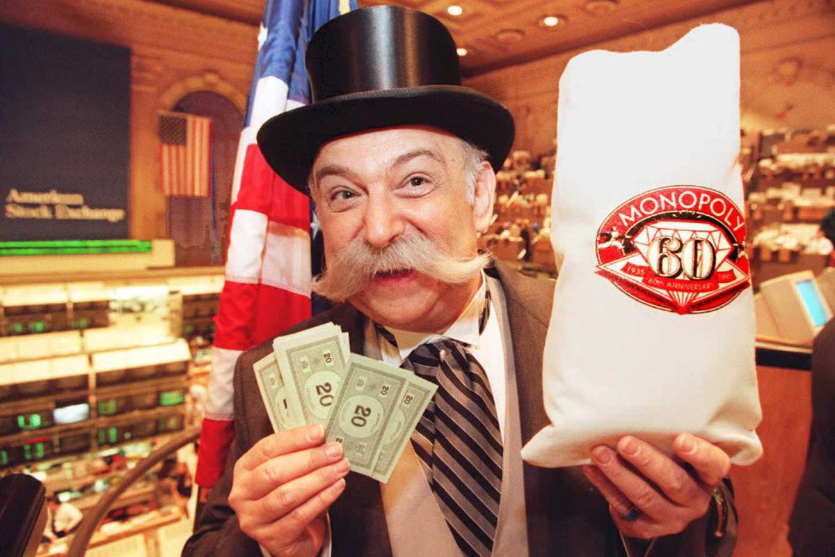 A person dressed up as Mr. Monopoly, holding up Monopoly money and a money bag commemorating the 60th anniversary of the game.