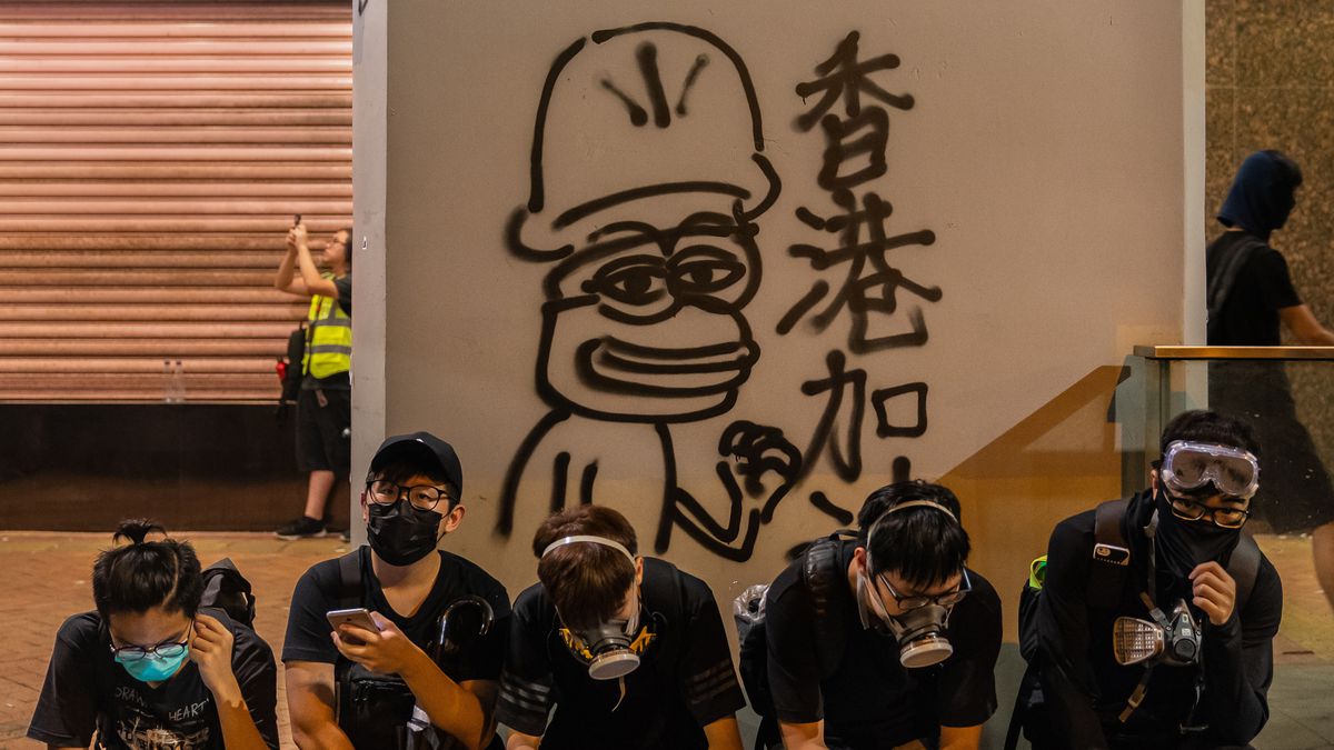 Masked Hong Kong protesters sit in front of graffiti of Pepe the Frog