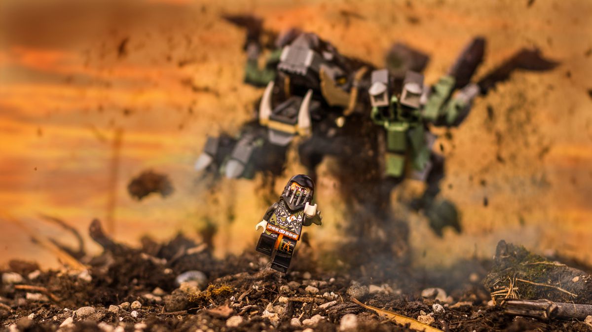 A ninja Lego minifig being chased by a lego-built monster flinging dirt in the air as its claw reaches forward