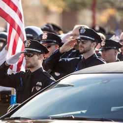 Police officers salute as the casket is carried to the graveside service for West Valley police officer Cody Brotherson at Valley View Memorial Park in West Valley City on Monday, Nov. 14, 2016.