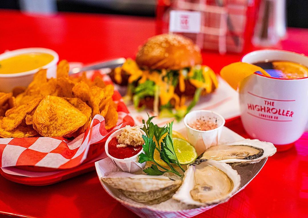 Oysters and other snacks sit on a red table, along with a drink in a mug that says the Highroller Lobster Co.
