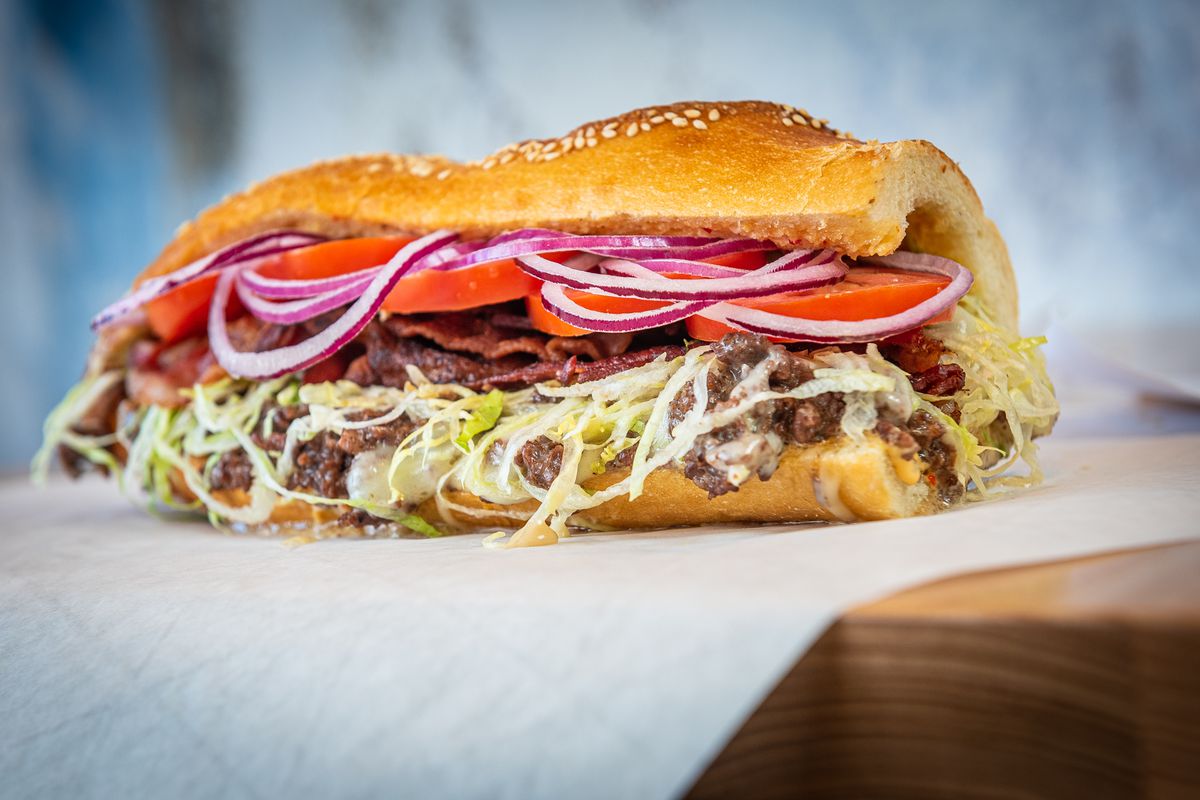 A Philly Special cheesesteak from Grazie Grazie shows off layers of grass-fed beef, Cooper sharp provolone, lettuce, red onion, and tomato on a golden roll