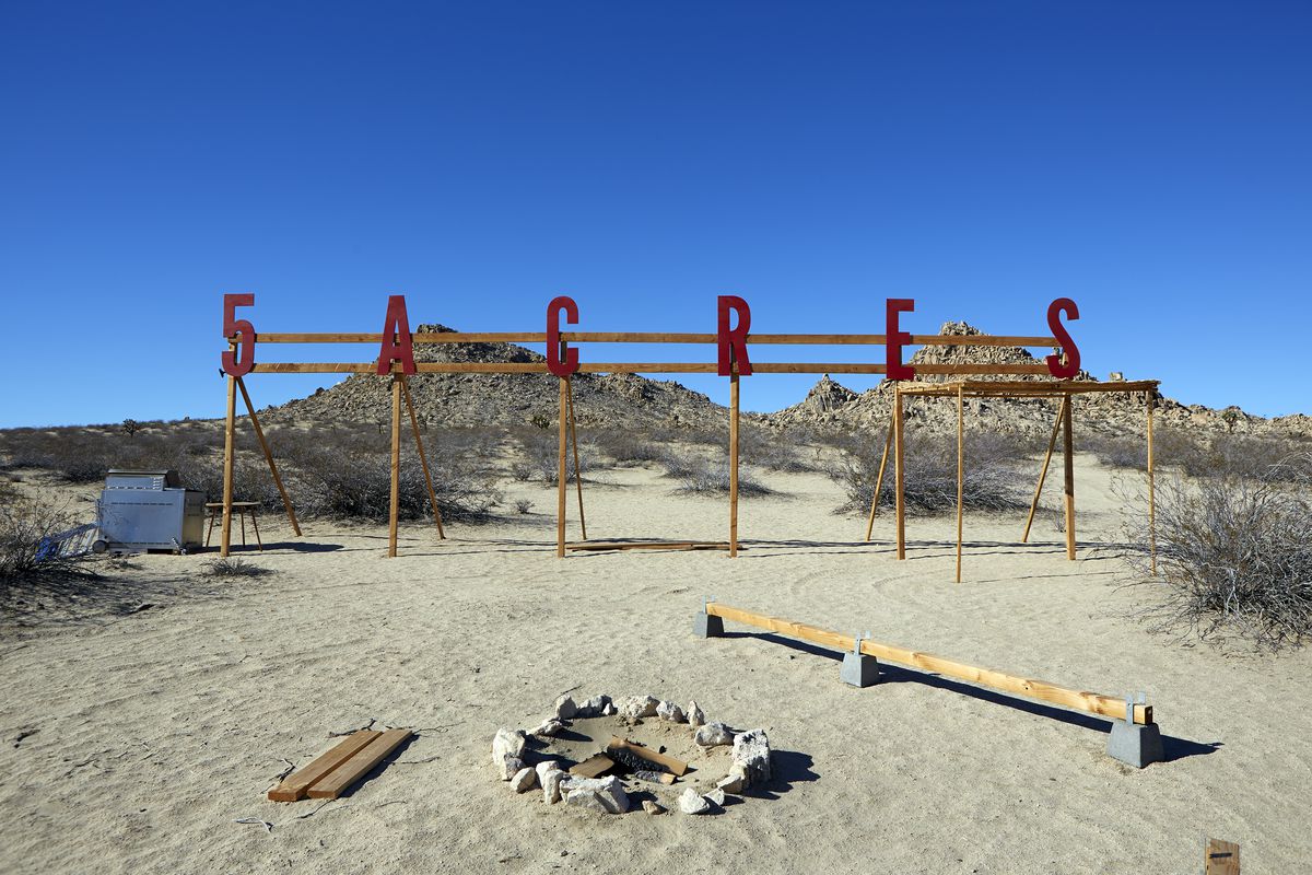 The space at 5 Acres, a sign that says 5 Acres in red, with a fire pit, surrounded by desert. 