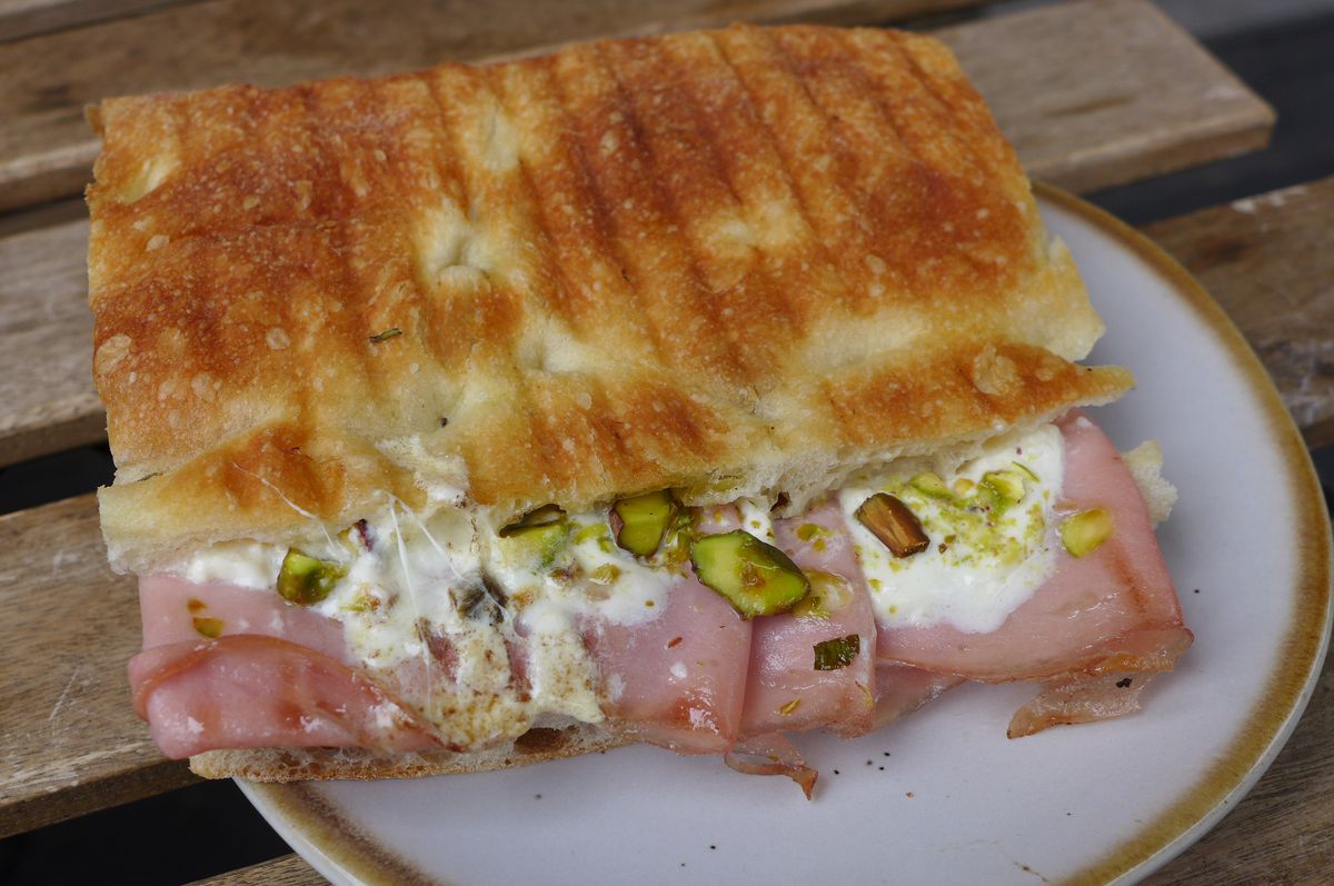 A focaccia sandwich with pink sliced meat and white dressing.