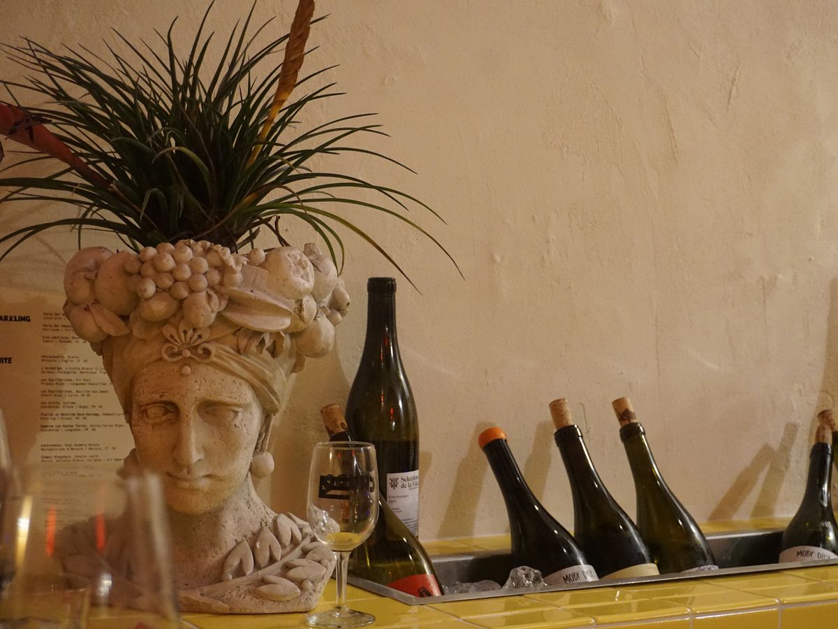 Corked wine bottles stick out of a hidden ice bucket along a wall. A bust of Frida Kahlo serving as a planter sits nearby