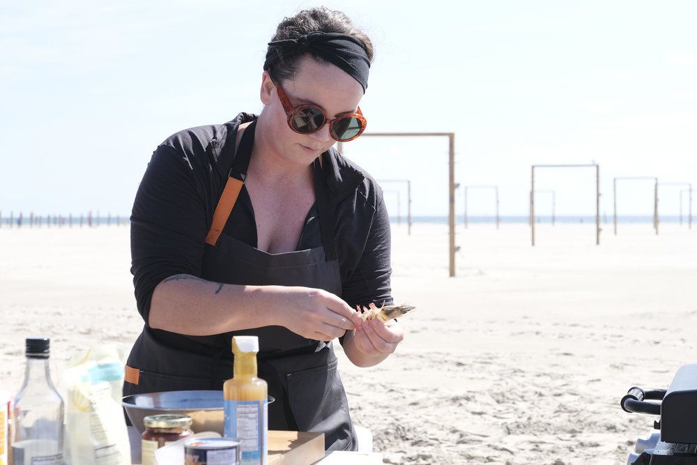 Chef Sarah Welch peeling a shrimp at her cooking station on the beach.