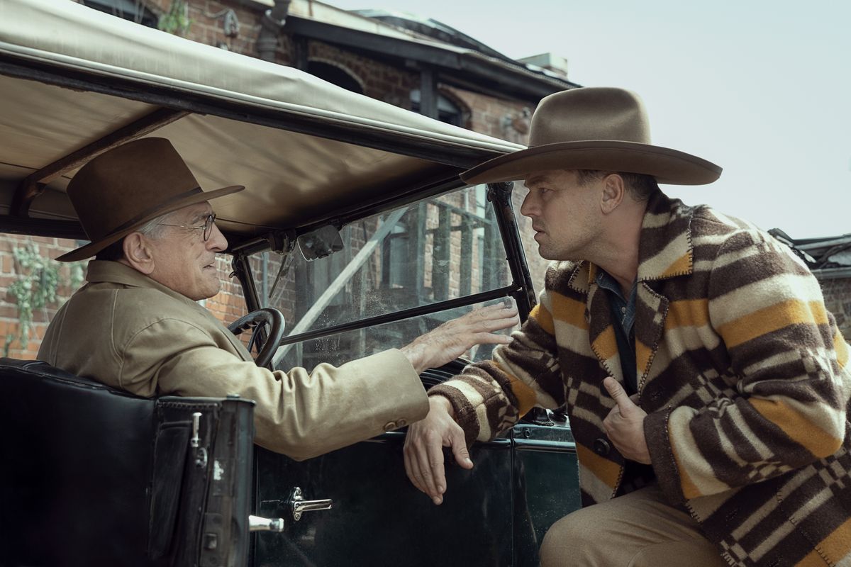 Leonardo DiCaprio, looking confused and wearing a cowboy hat and garish jacket, talks to Robert De Niro sitting in a car in Killers of the Flower Moon