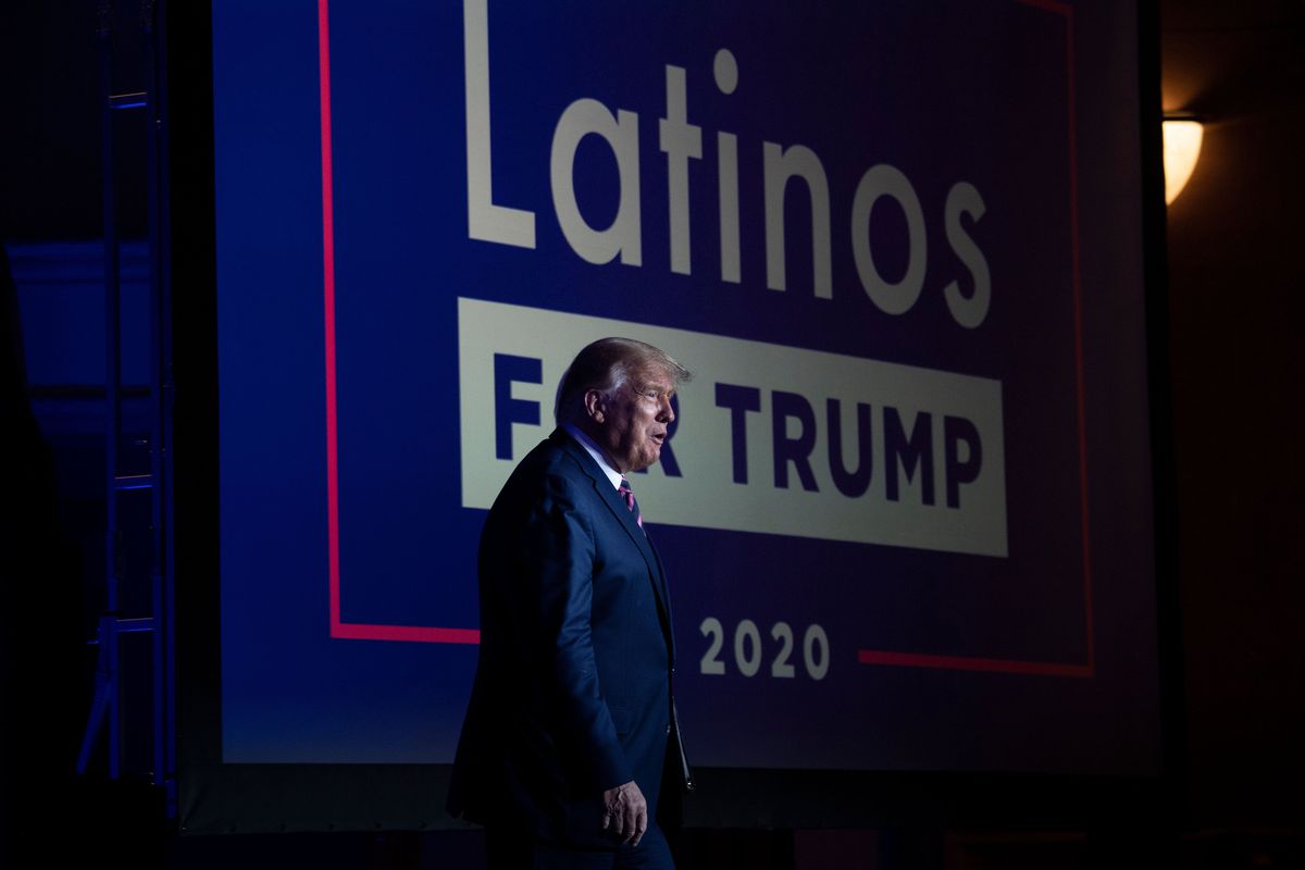 Trump stands in front of a sign that reads “Latinos for Trump 2020”