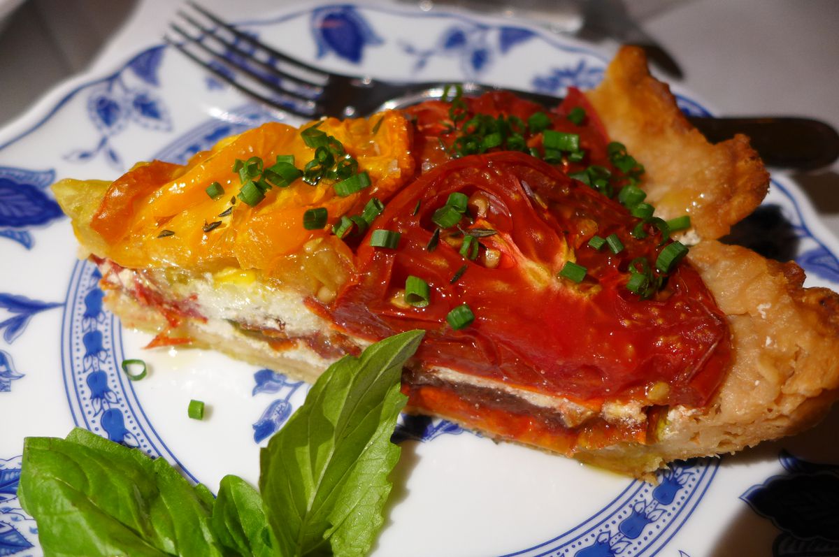 A slice of pie with red and yellow slice tomatoes as filling.