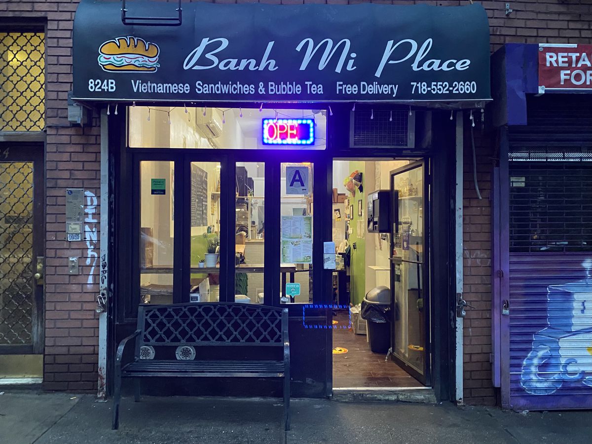 Outside of Banh Mi Place in Prospect Heights, a small Vietnamese takeout counter with a bench for outdoor seating.