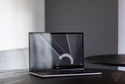 The Asus Chromebook CX5 open, tilted to the right, on a table with a gray and white background.  The screen displays a black, white and gray desktop pattern.