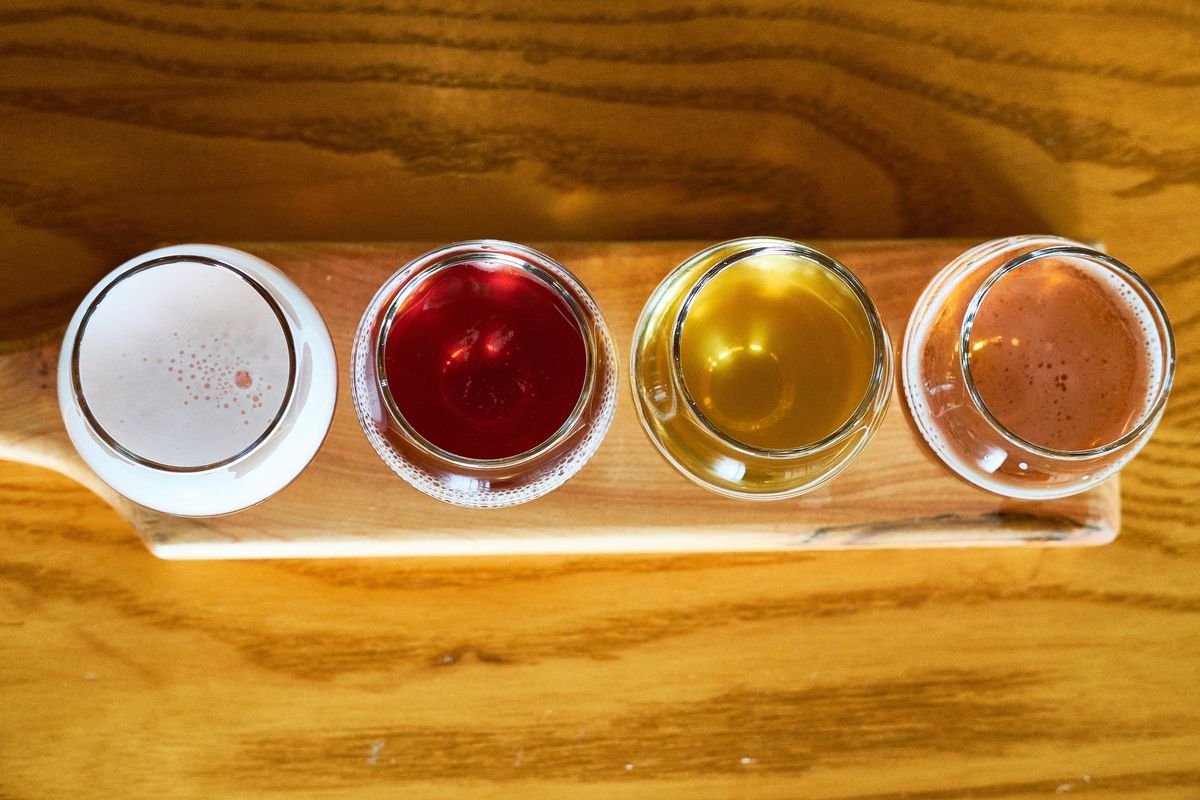 A flight of four small, colorful sour beers lined up on a tasting board sitting on a wooden table at Cascade Brewing Barrel House.