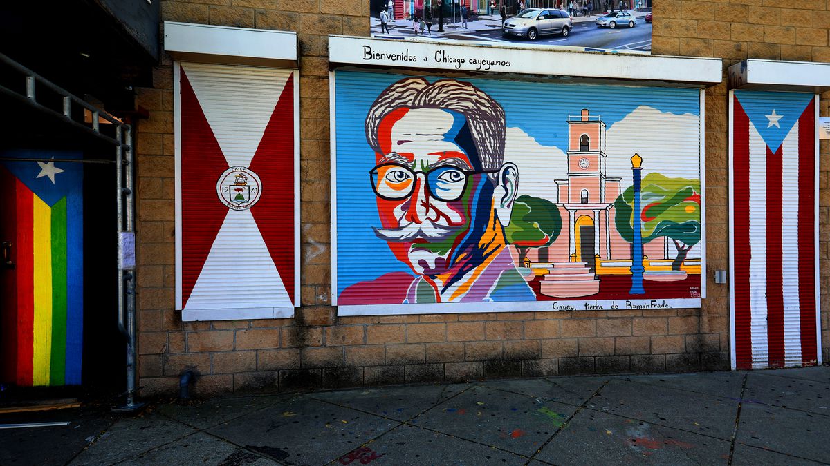 Colorful murals painted on the side of a building - a mans face with many colors included, a building, and a Puerto Rican flag.