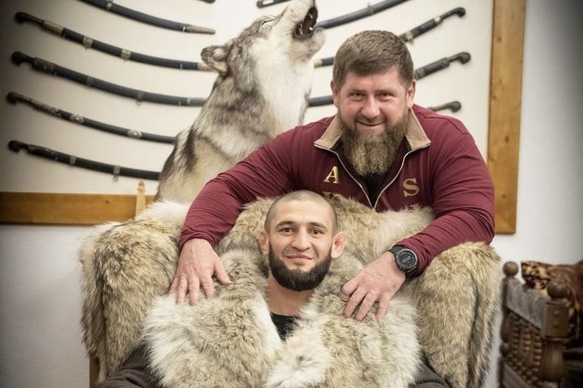 A picture of Ramzan Kadyrov posing behind UFC star Khamzat Chimaev, who is dressed in a fur coat with a statue of a wolf behind him 