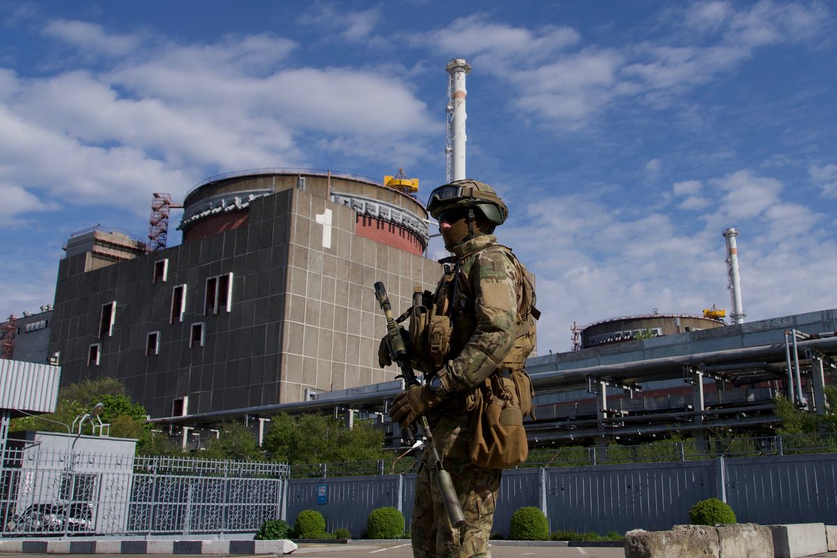 A Russian serviceman in combat vest and helmet holds a machine gun in front of the Zaporizhzhia nuclear power plant.