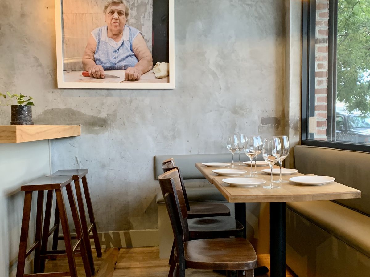 Chairs and bar stools are pulled up to blonde-colored furniture and a bar top inside of Popina, a restaurant in Cobble Hill.
