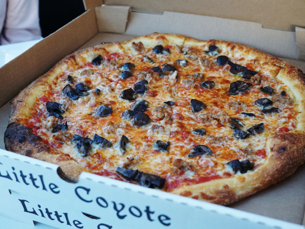 A stack of white boxes of pizza with olives on the topmost pie.