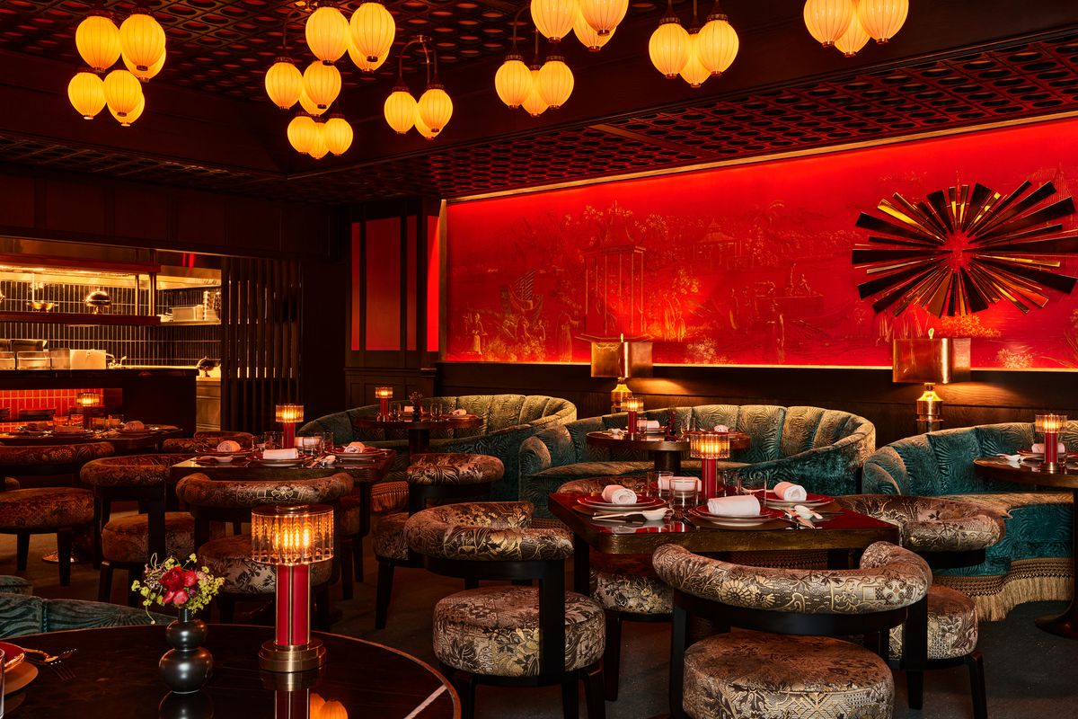 A Chinese restaurant dining room with cushy banquettes, a red cutout backdrop, and dim lighting.