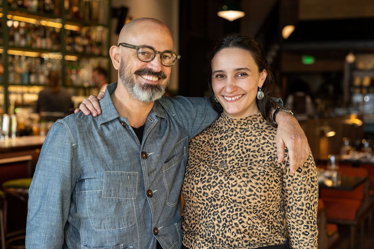 Dos hombres, un hombre en sambray y una mujer en un leopardo, están uno al lado del otro dentro de un nuevo restaurante.