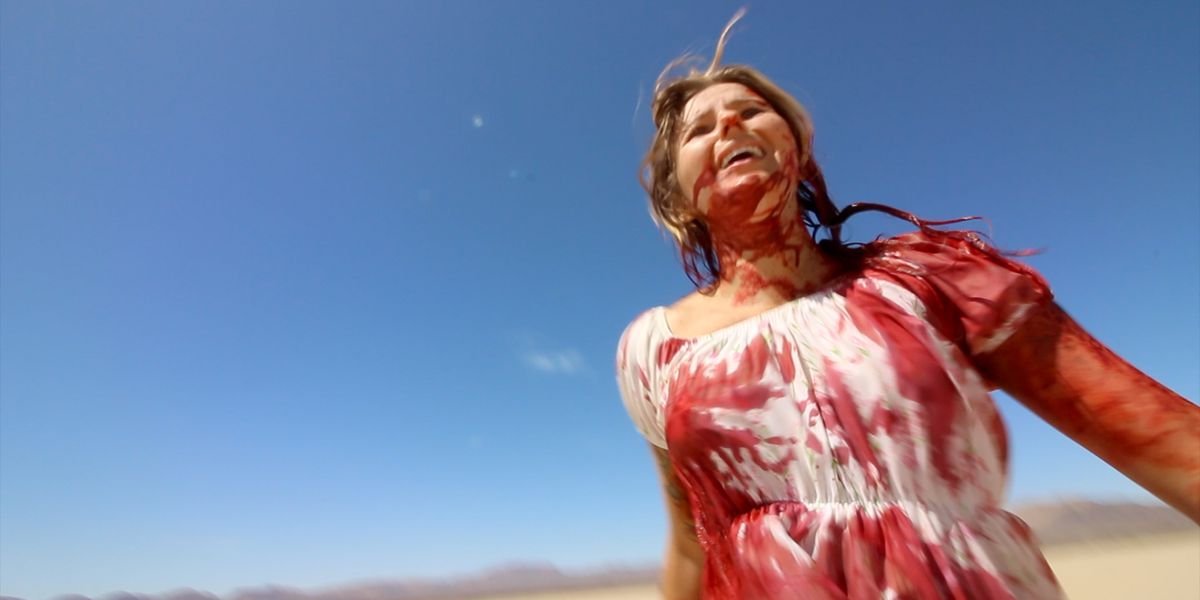 Michelle May walks through the desert smiling and covered in blood in The Outwaters