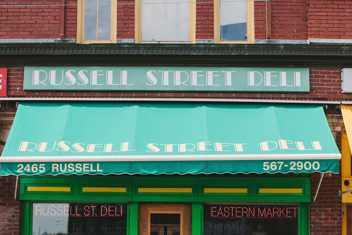 Customers gather outside of Russell Street Deli underneath bright green awnings on a sunny day at Eastern Market in Detroit.