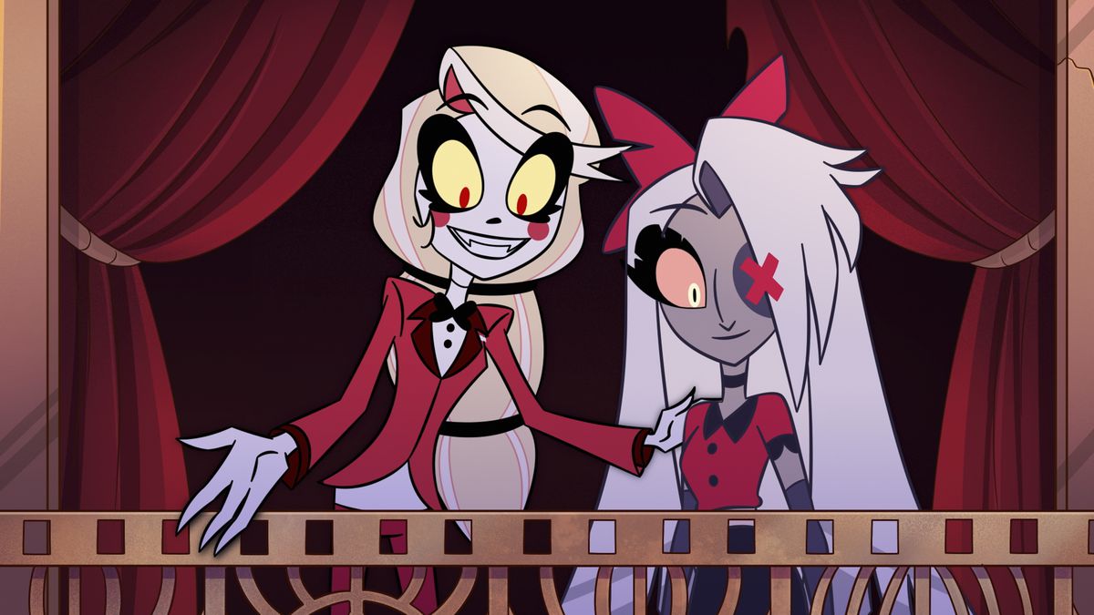 Charlie, a demon with pale skin and long blonde hair, shows Vaggie, a grey-skinned demon with white hair, something while standing in front of a red curtain