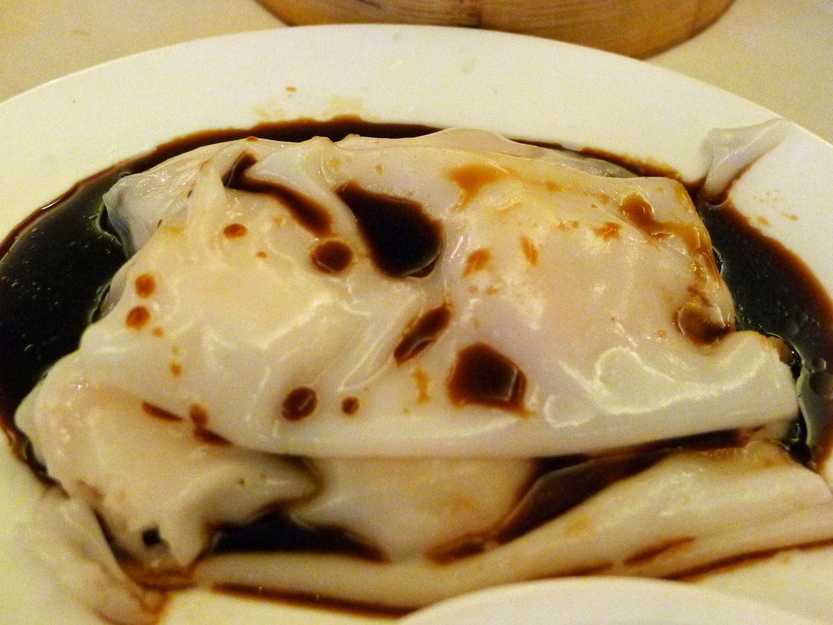 Shrimp rice noodle rolls on a white plate inundated with dark soy sauce.