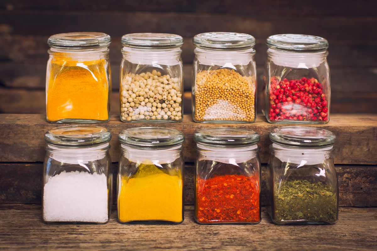 Two rows of spices in glass containers on a wooden shelf