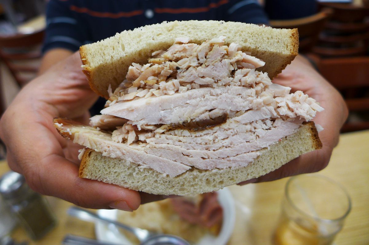 A piled high on rye turkey sandwich held by a pair of hands...
