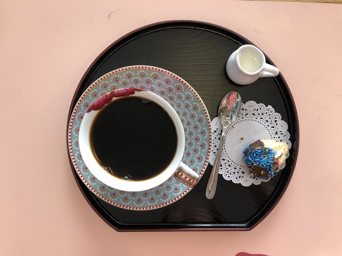 a cup of black tea on a decorative plate with a doily and cookie with sprinkles to the right