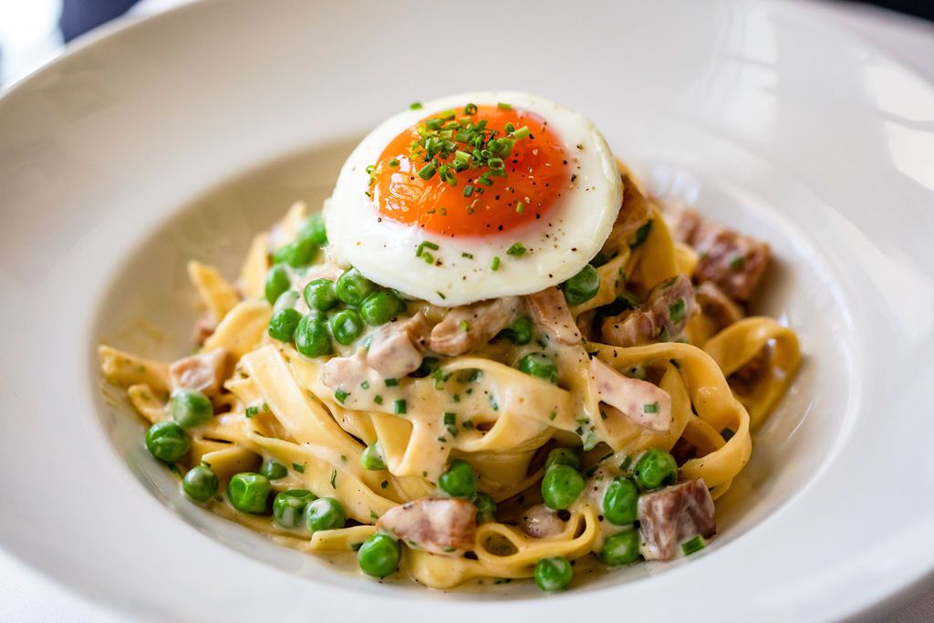 A plate of carbonara pasta topped with a country egg.