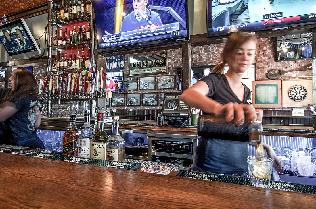 A server pours a drink at an Irish bar as TVs play in the background.