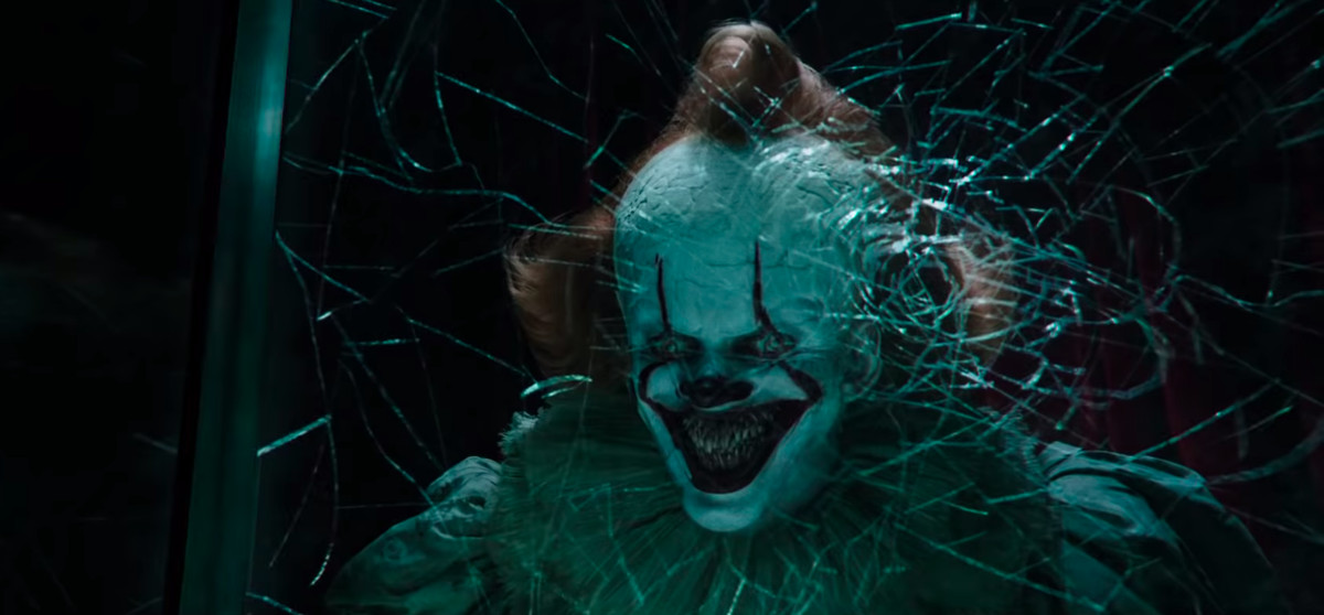 The scary clown in the movie “It Chapter Two” grins from behind a sheet of shattered glass.