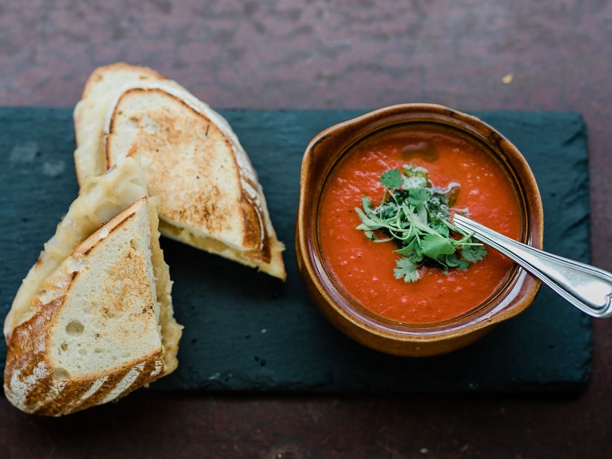 From above, a bowl of tomato soup beside a sliced grilled cheese