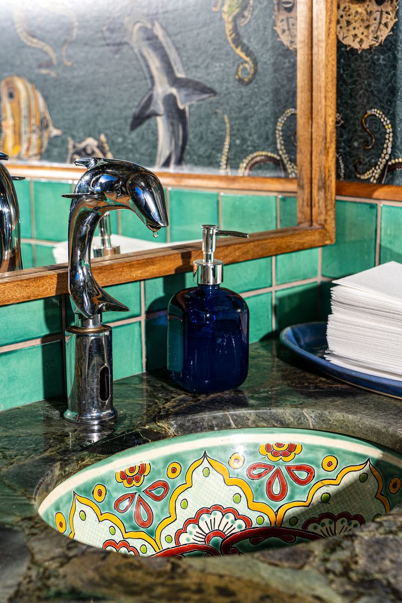 A colorful bathroom sink includes a silver dolphin-shaped faucet. 