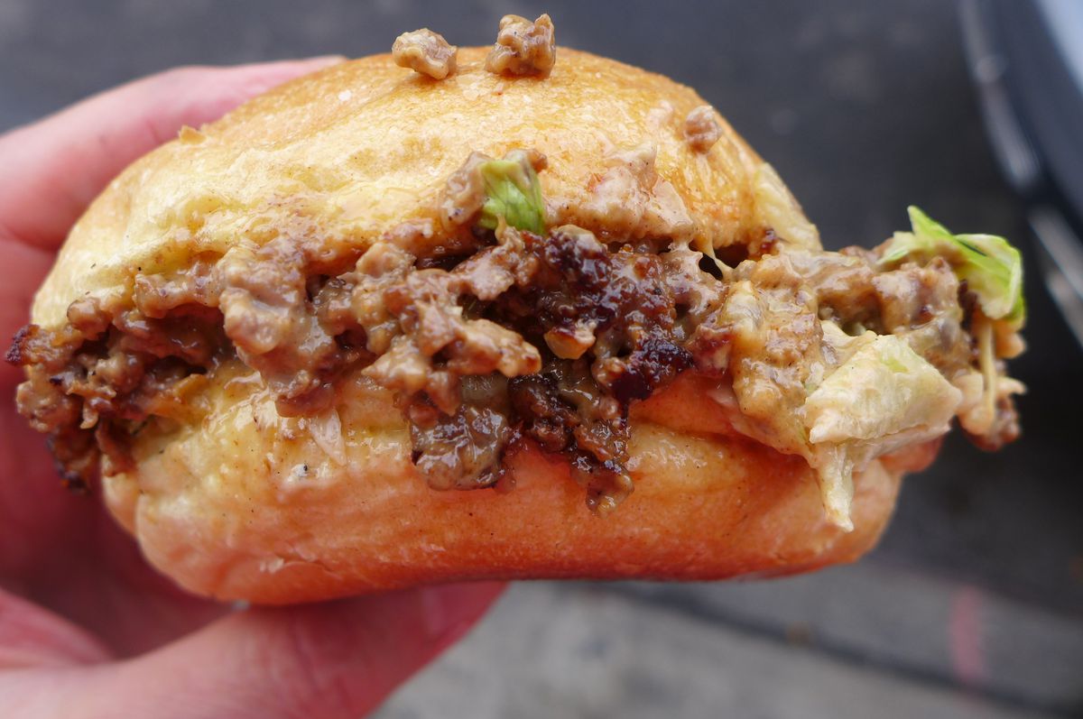 A hand holds a small bun with ground beef and yellow cheese visible on the sidea.