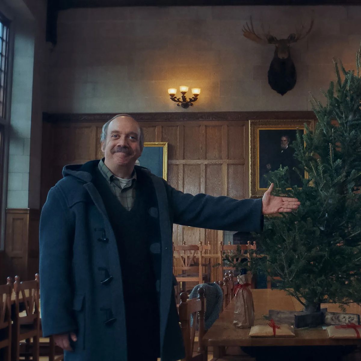Paul Giamatti gesturing towards a tree in a large room in The Holdovers.
