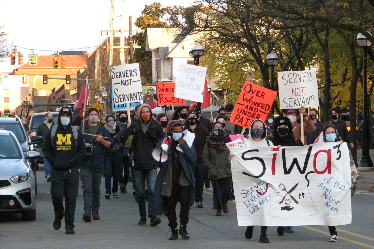 A photo of masked protesters from SIWA3 marching through the streets of Ann Arbor. Some hold signs reading “Servers, Not Servants.”