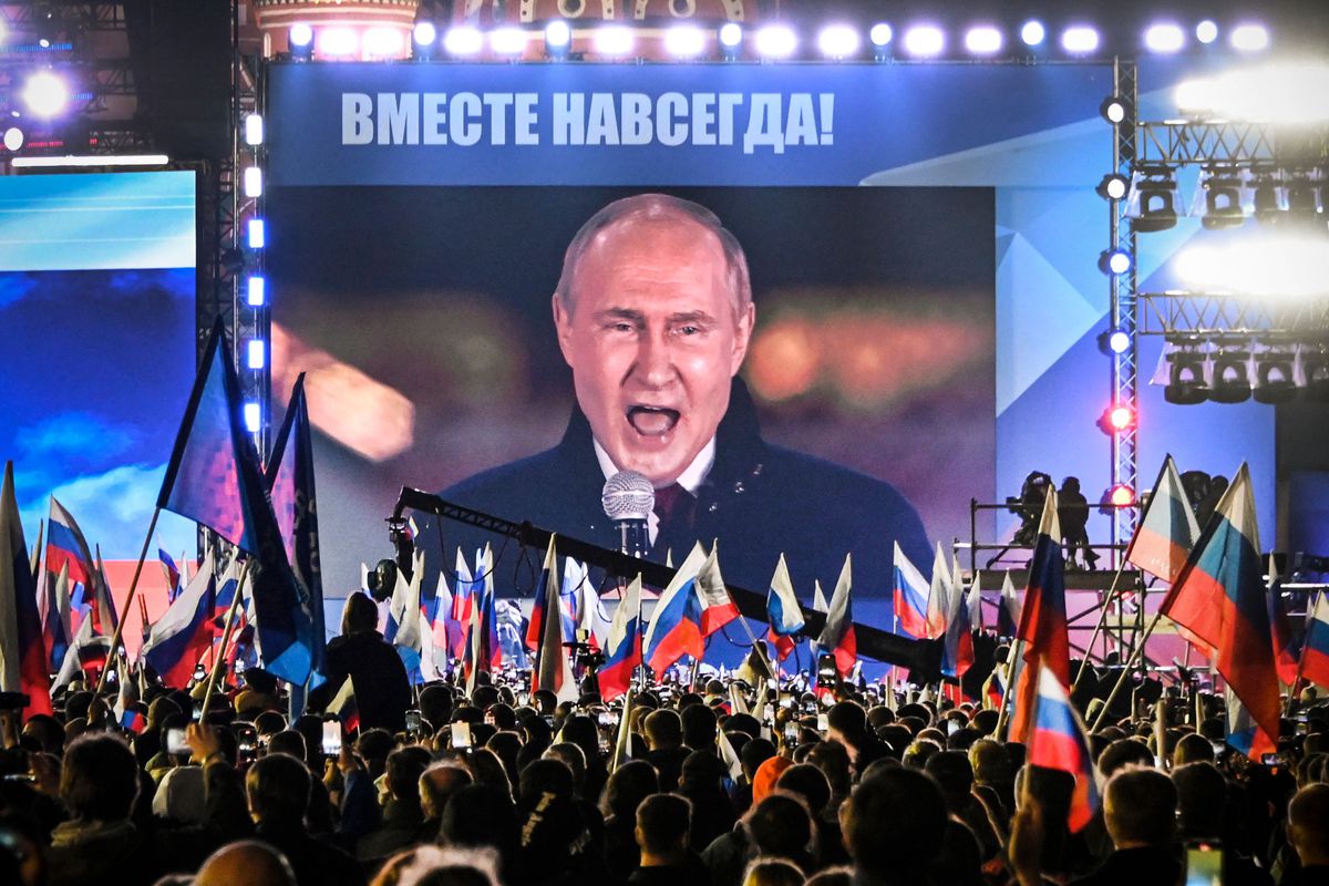 Russian President Vladimir Putin is seen on a large projection screen in Moscow’s Red Square as he addresses a rally and concert. The crowd is full of people waving Russian flags, and Putin appears to be shouting.