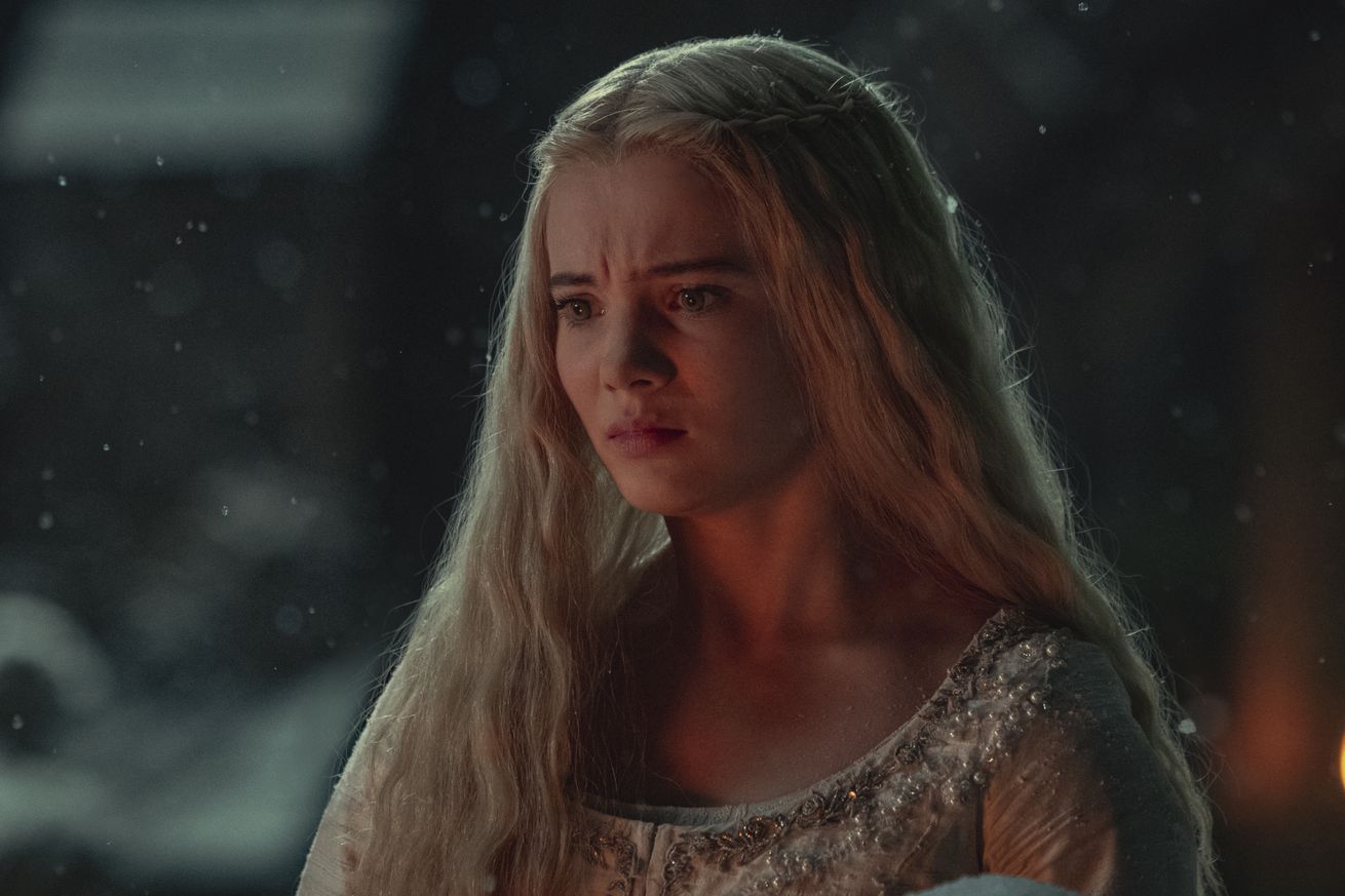 A girl in a nightgown standing outside in the snow and frowning.
