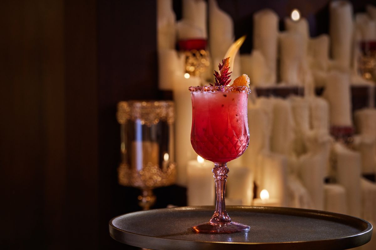 A bright red cocktail with garnishes in a crystal goblet.