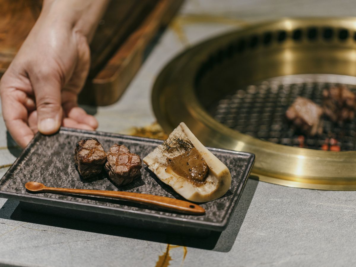 A chef holds a small plate of grilled beef.