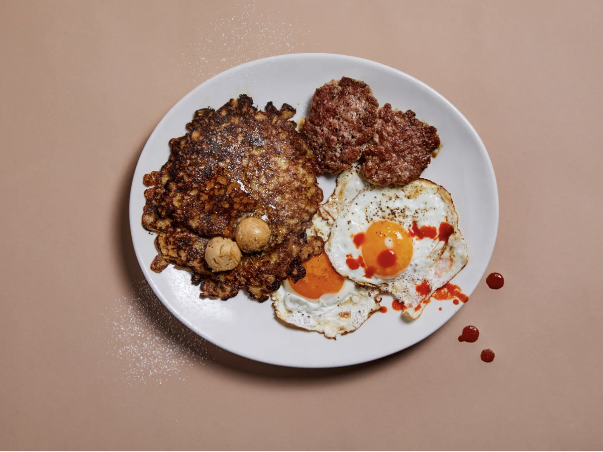 Griddle cakes with cinnamon butter as well as eggs, and sausage on a white plate atop a tan background at the Santa Monica location of Breakfast by Salt’s Cure.