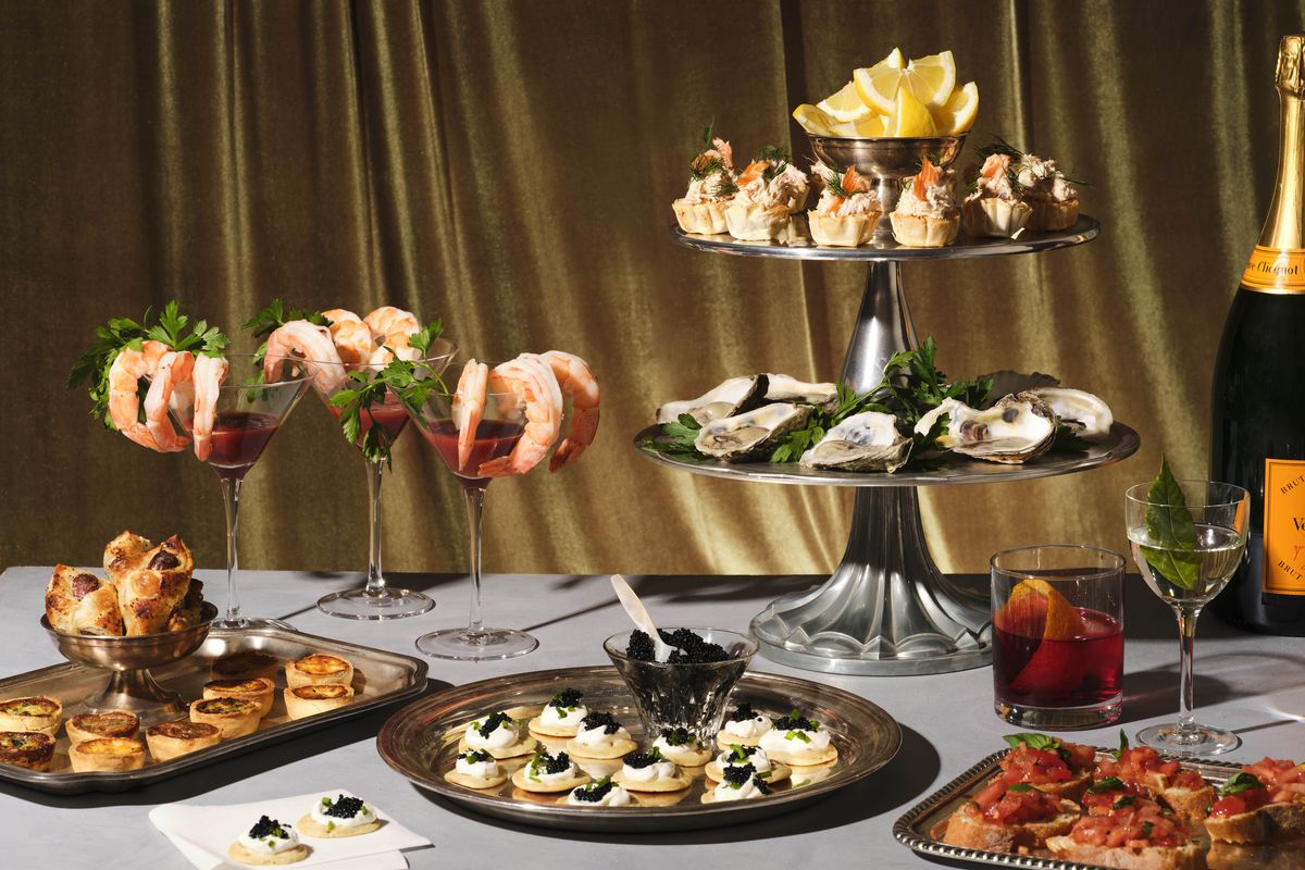 A table set with an array of appetizers, including shrimp cocktail, oysters, blinis, and canapes.