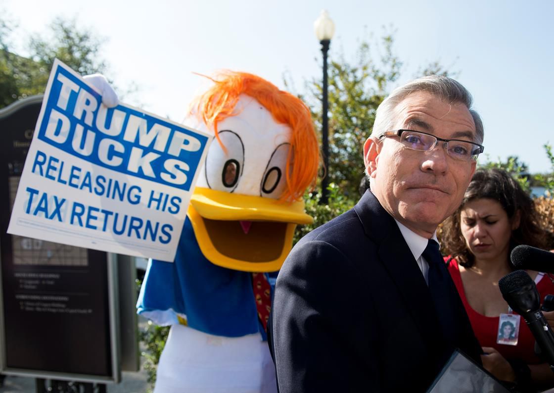 Man dressed as duck holding sign that says "Trump ducks releasing his tax returns"