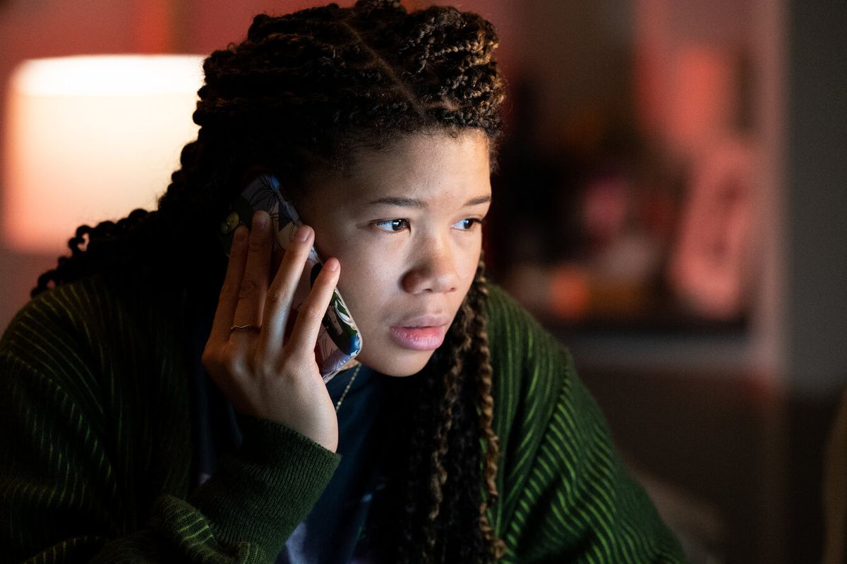 A young woman (Storm Reid) with braided hair holding a cell phone to her ear while staring at a screen off-screen in “Missing.”