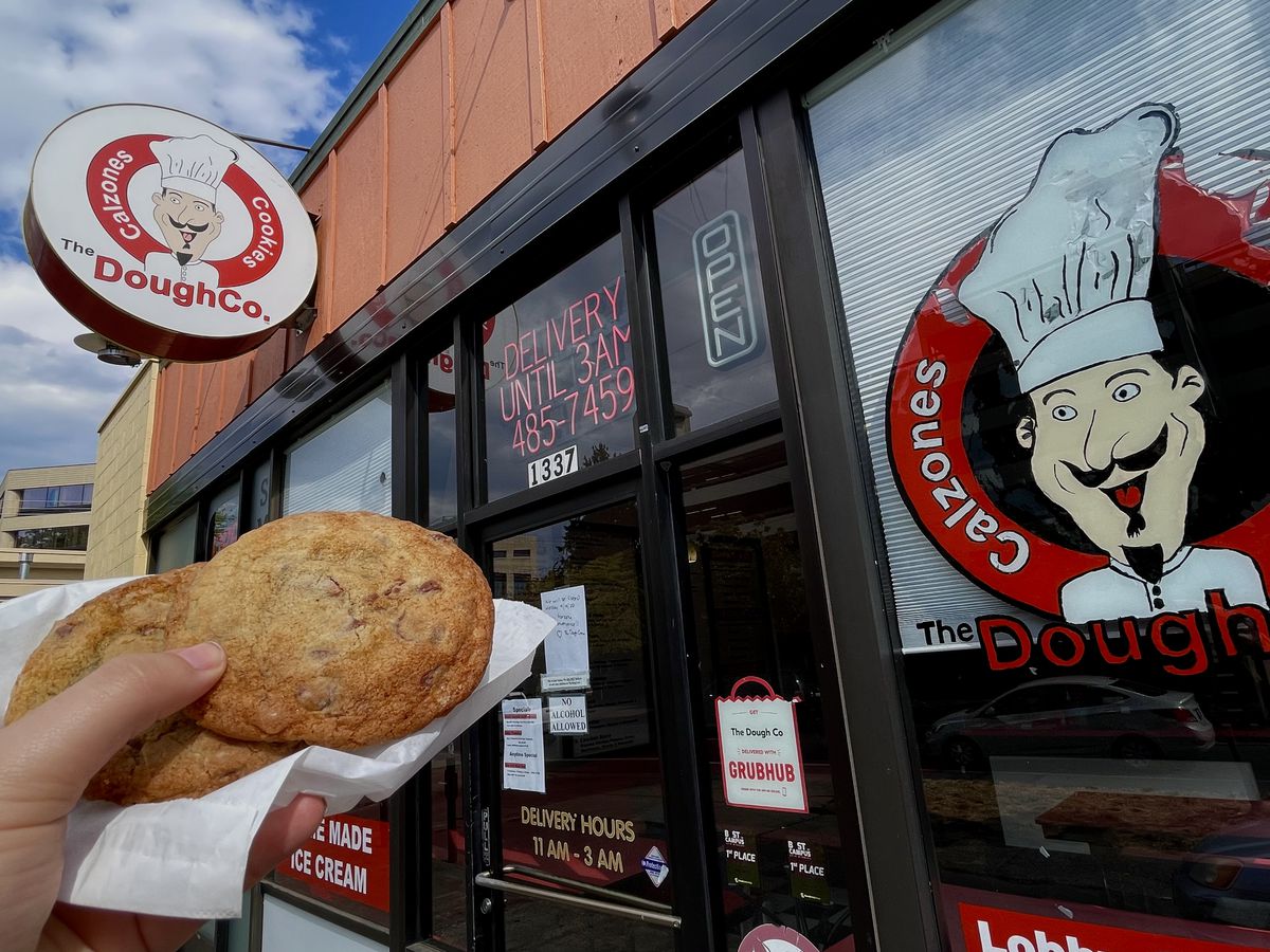 A hand holds two cookies in front of Dough Co’s facade.