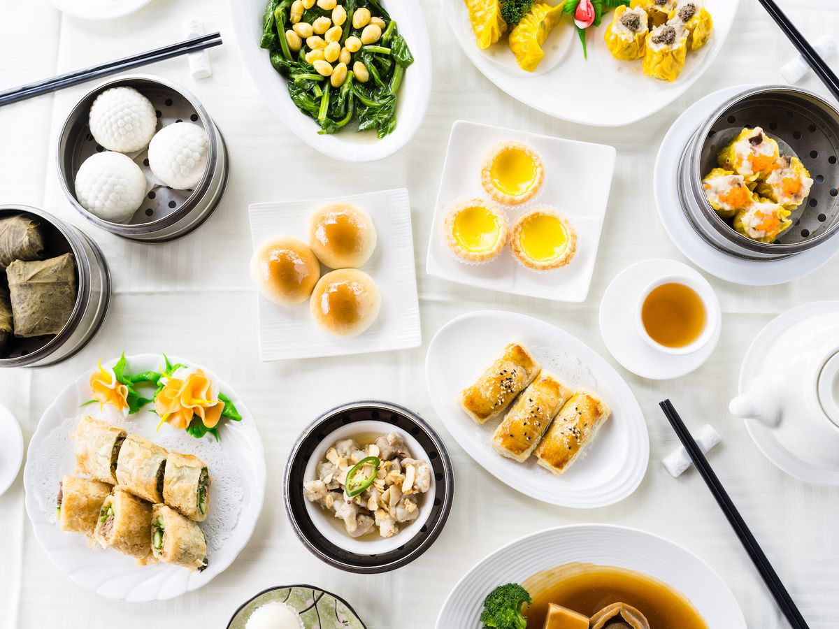 An overhead shot of a white tablecloth table with lots of dim sum options on plates and in tins.