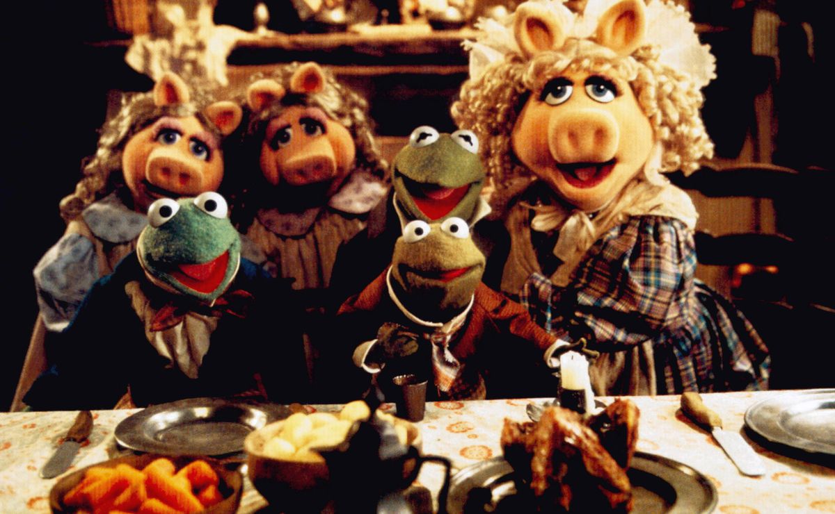 Kermit, Piggy, Robin, and other muppets, costumed and posing at the dinner table as the Cratchit family in The Muppet Christmas Carol.